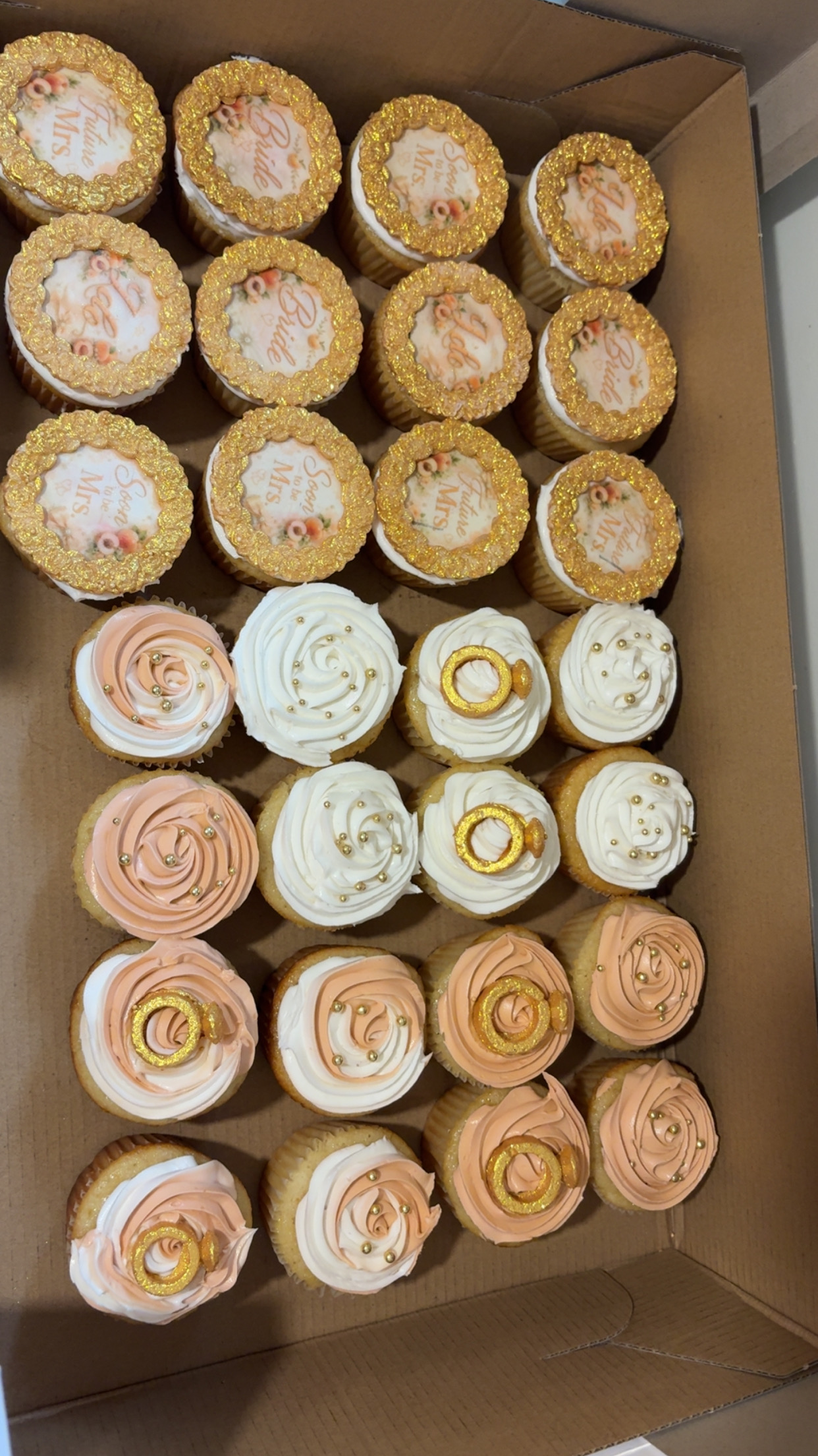 Two dozen gold and rose cupcakes in a box