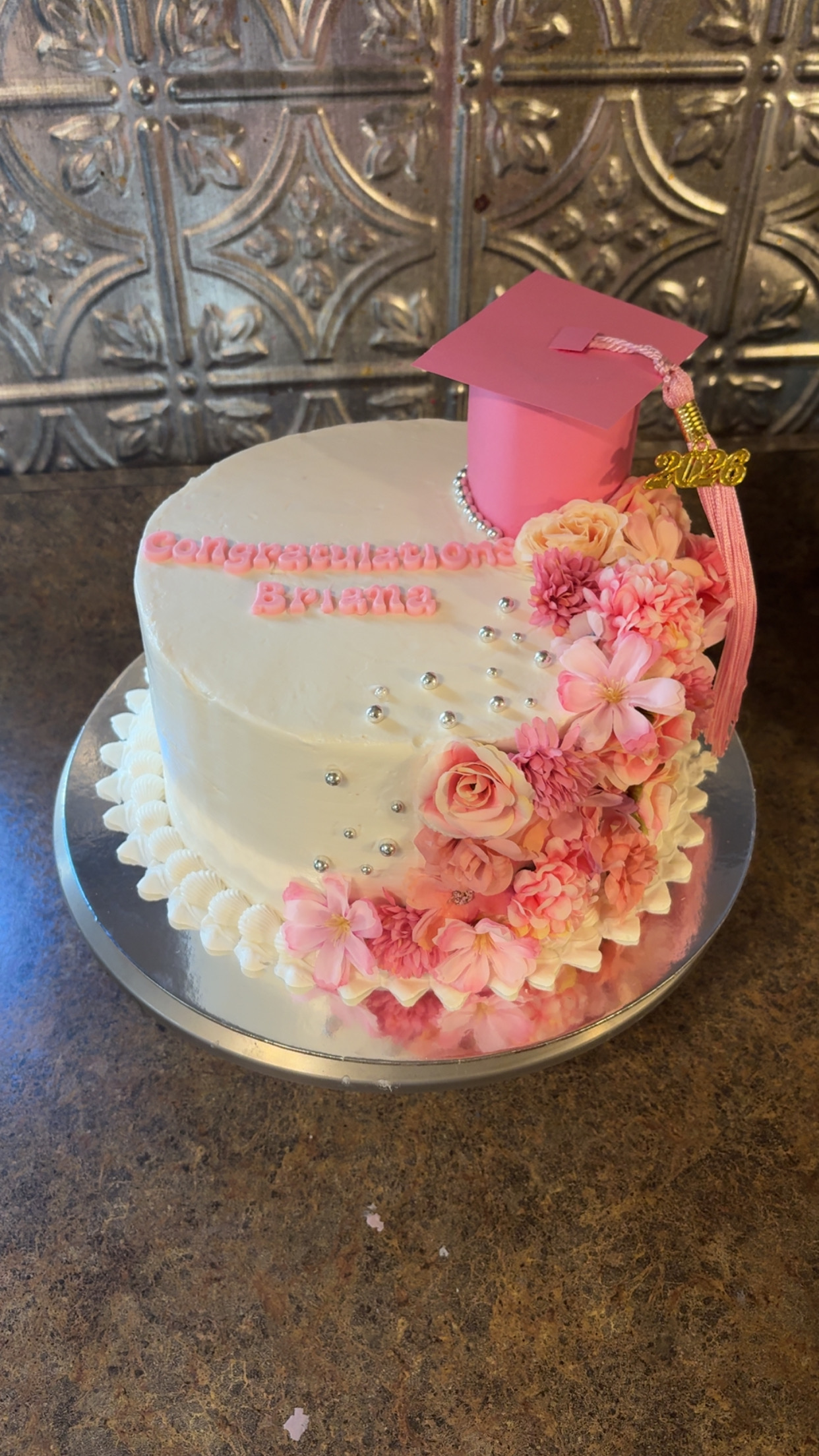 White graduation cake with pink flower details and cap topper — a Desire Delights creation